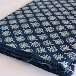 May include: A folded stack of indigo blue cotton fabric with a white floral pattern. The fabric is folded in thirds and has a white tag with the text "ShiboriNTieDye" on the bottom right corner.