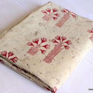 May include: A folded piece of off-white fabric with a red tree pattern. The fabric has a slightly textured surface.