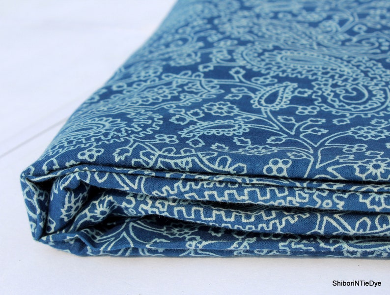 May include: A folded blue fabric with a white paisley pattern. The fabric is soft and has a subtle sheen.