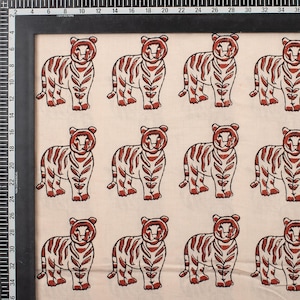 May include: Cream-colored fabric featuring a repeating pattern of stylized tigers. Each tiger is depicted in a standing pose with red-brown stripes and details. The fabric is framed with a black border and includes a centimeter ruler.