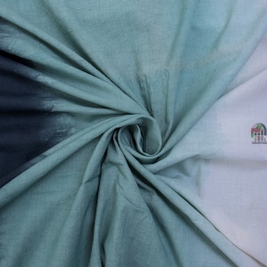 Może przedstawiać: Skręcona, teksturowana tkanina z gradientem kolorów. Tkanina przechodzi od głębokiego granatowego do odcieni turkusu i jasnej bieli. Materiał jest złożony i udrapowany, prezentując wariacje kolorystyczne.