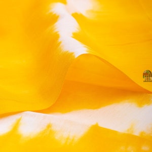 May include: Close-up of a yellow fabric with white tie-dye patterns. The fabric is soft and flowing, creating a gentle wave.