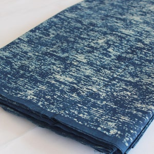 May include: A folded piece of blue and white fabric with a tie-dye pattern. The fabric has a textured, slightly rough surface.