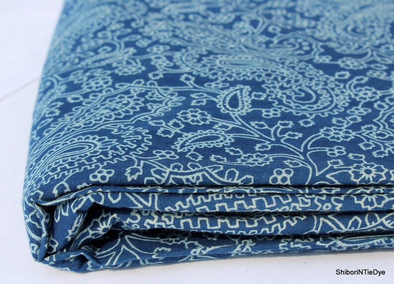 May include: A folded piece of blue fabric with a white paisley pattern. The fabric is folded in thirds and the edges are visible.