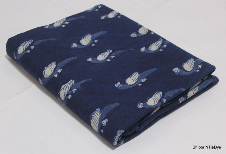 K&ouml;nnte beinhalten: Ein gefaltetes St&uuml;ck indigo-blauer Baumwollstoff mit einem wei&szlig;en, gedruckten Muster aus stilisierten V&ouml;geln.