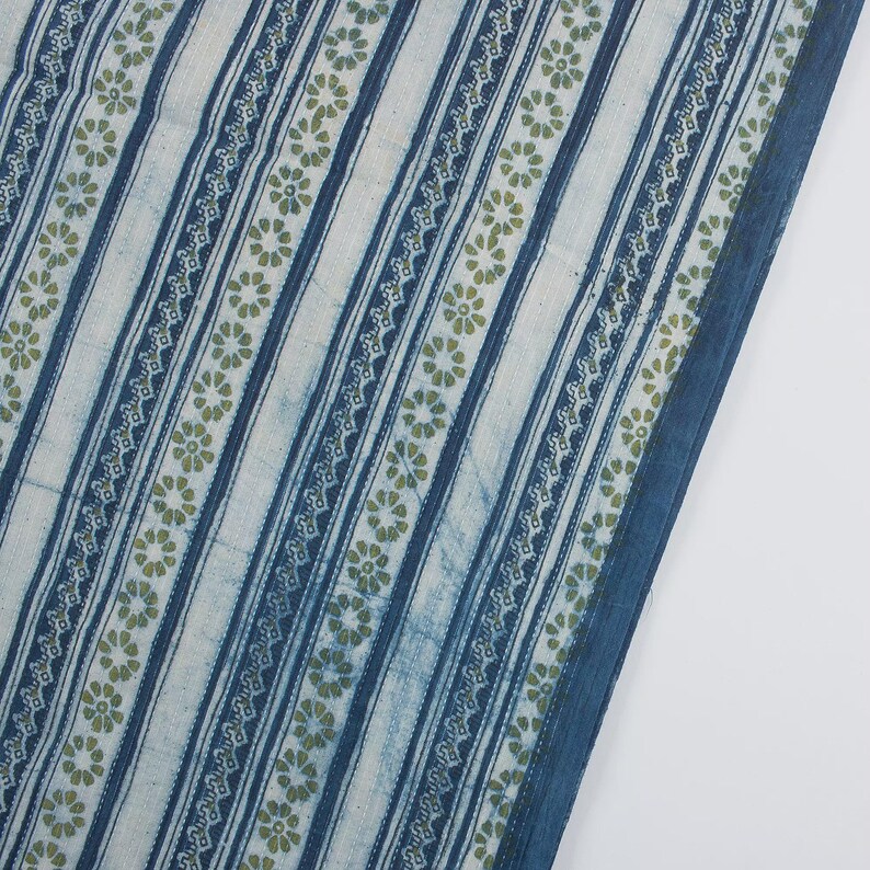 May include: A textile with a repeating pattern of vertical stripes in white and indigo blue. The stripes are accented with rows of small, olive-green floral motifs and decorative borders. The fabric has a slightly faded appearance, suggesting a vintage or handcrafted quality.