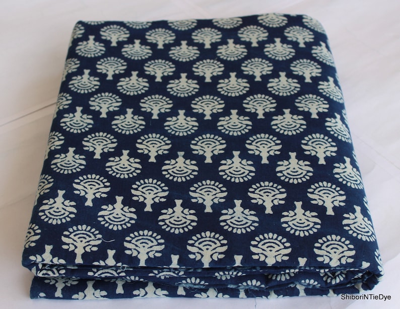 May include: A folded piece of indigo blue cotton fabric with a white floral pattern. The fabric is printed with a repeating design of stylized trees.
