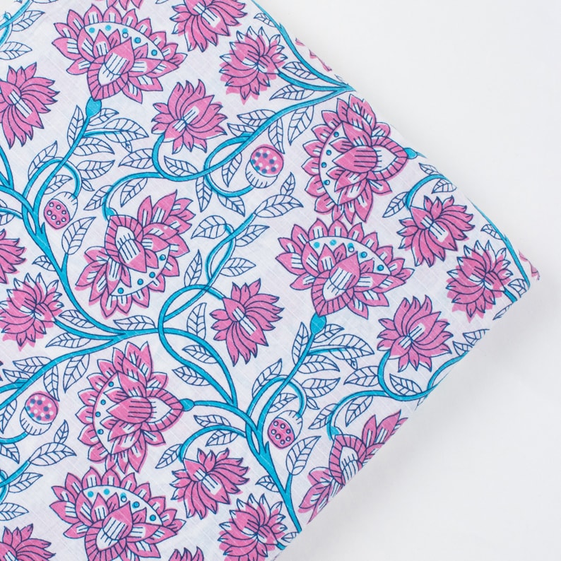 May include: White fabric with a pink and blue floral pattern. The fabric features a repeating design of stylised flowers with intricate details.