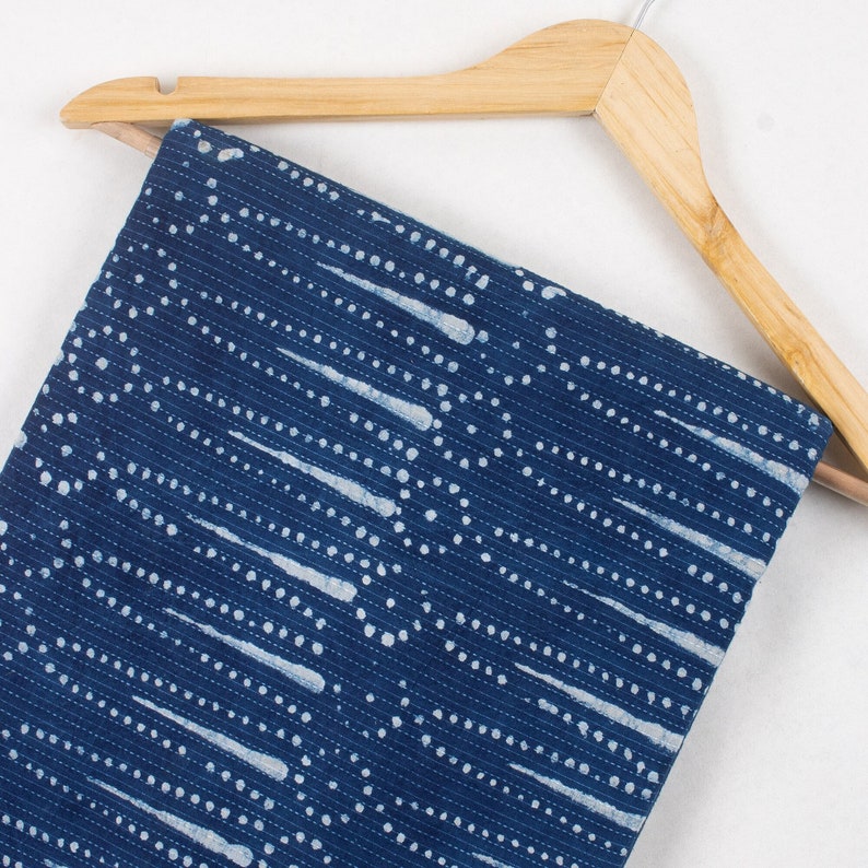 May include: A blue fabric with a white pattern of dots and lines. The fabric is hanging on a wooden hanger.