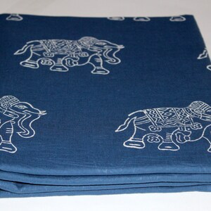 May include: A folded blue cotton fabric with a white elephant print. The fabric has a textured surface and is folded in thirds.