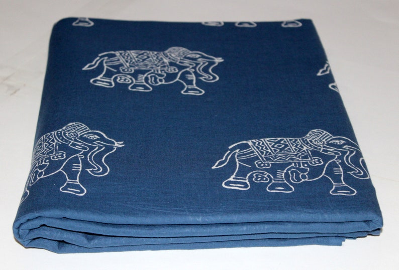 May include: A folded blue cotton fabric with a white elephant print. The fabric has a textured surface and is folded in thirds.