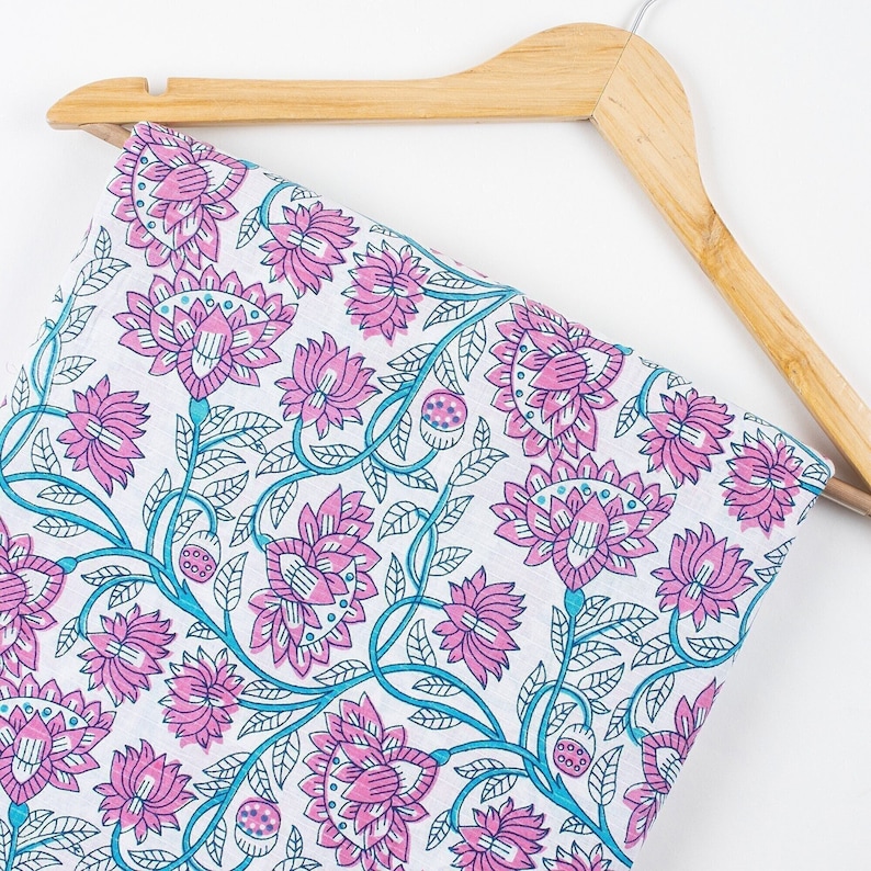 May include: White fabric with a pink and blue floral print. The fabric is draped over a wooden hanger.