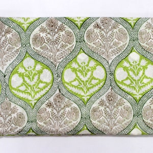 May include: White cotton fabric with a green and brown floral print. The pattern features repeating teardrop shapes with a floral design inside. The fabric is folded in half.