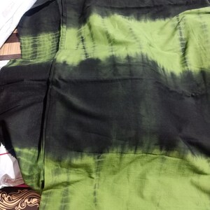 Op de afbeelding: Groen en zwart tie-dye stof met een gestreept patroon. De stof is gevouwen en heeft een textuur.