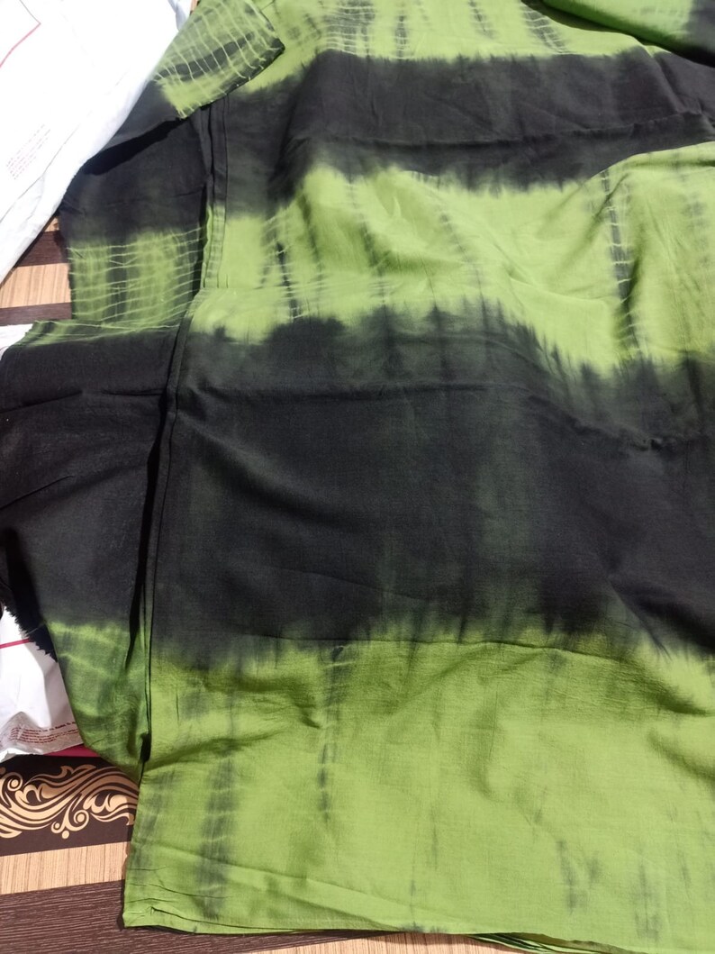 Op de afbeelding: Groen en zwart tie-dye stof met een gestreept patroon. De stof is gevouwen en heeft een textuur.