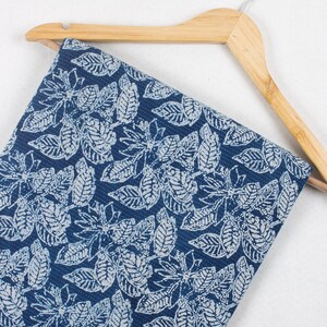May include: A blue fabric with a white leaf pattern. The fabric is hanging on a wooden hanger.