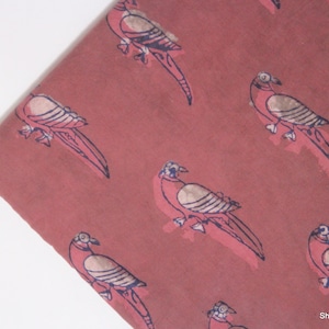 以下が含まれることがあります： ピンク色の綿生地に、青と白の鳥が繰り返し描かれた模様。鳥はスタイリッシュでシンプルなデザインです。