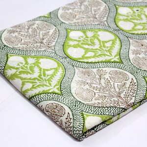 May include: White cotton fabric with a green and brown floral print. The print features a repeating pattern of teardrop shapes with floral designs inside. The fabric is folded in half.