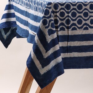 May include: A blue and white cotton tablecloth with a geometric pattern. The tablecloth is folded and draped over a wooden table.