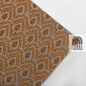 May include: A brown fabric with a white and black floral pattern. The fabric has a repeating pattern of small leaves and flowers.