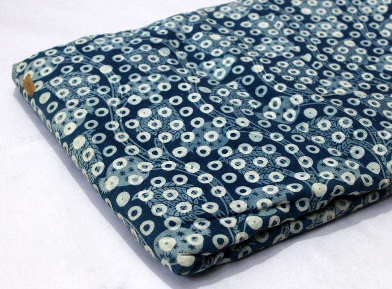 May include: Blue fabric with a white pattern of circles and leaves. The fabric is folded in half.