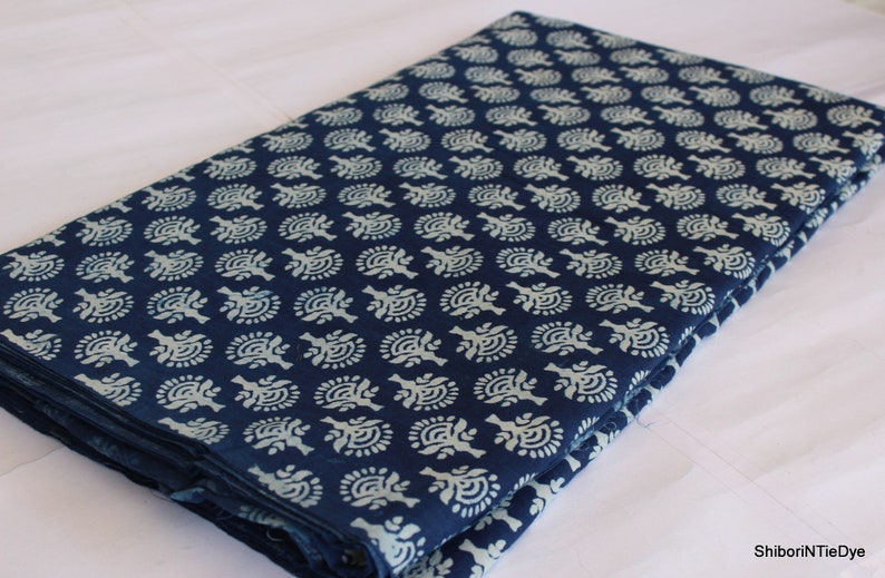 May include: A folded piece of indigo blue fabric with a white floral pattern. The fabric is folded in half and the pattern is visible on both sides.
