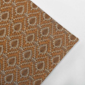 May include: A brown fabric with a repeating pattern of white and black floral designs. The fabric has a subtle sheen and a soft texture.