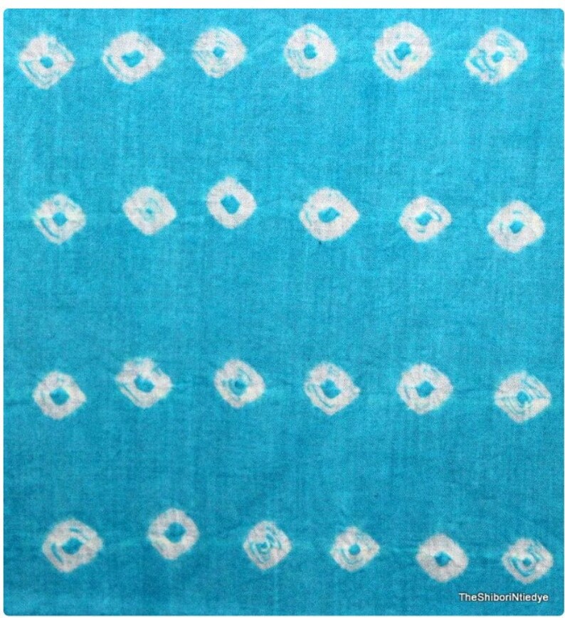 May include: A turquoise blue fabric with a white shibori tie-dye pattern. The pattern is made up of small, white circles.