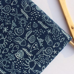 Puede incluir: Tela de algodón azul con un patrón blanco de vida marina. El patrón incluye peces, cangrejos, estrellas de mar, conchas marinas y algas.