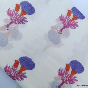Puede incluir: Tela blanca con un estampado floral repetido. El dise&ntilde;o presenta flores moradas, naranjas y rosas con estructuras detalladas en forma de hojas. Las flores destacan sobre un fondo blanco liso, creando un contraste llamativo.