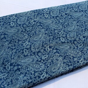 May include: A blue fabric with a white paisley pattern. The fabric is folded in half and has a white border.