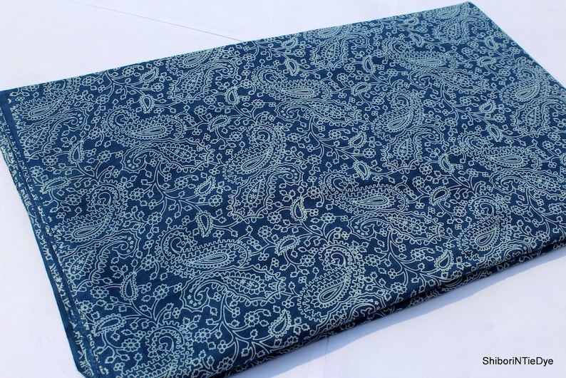 May include: A blue fabric with a white paisley pattern. The fabric is folded in half and has a white border.