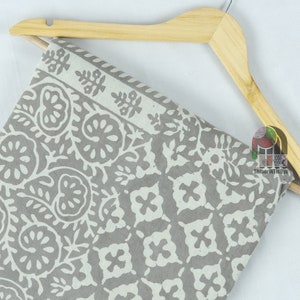 May include: A gray and white cotton fabric with a floral pattern. The fabric is folded and draped over a wooden hanger.