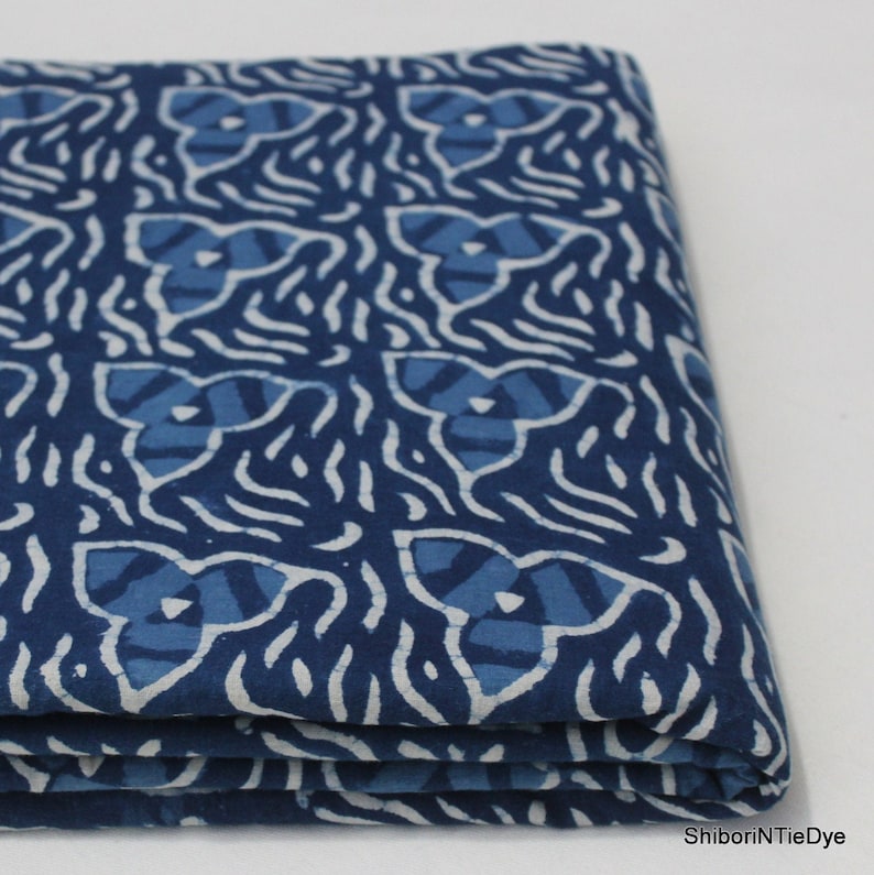 May include: A folded blue and white cotton fabric with a repeating pattern of stylized flowers. The fabric is a traditional Indian hand-block printed design.