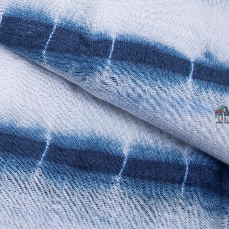 Op de afbeelding: Close-up van een witte stof met blauwe tie-dye strepen. De stof heeft een textuur, geweven uiterlijk.