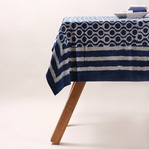 May include: A blue and white patterned tablecloth with a geometric design. The tablecloth is draped over a wooden table with a single leg visible.