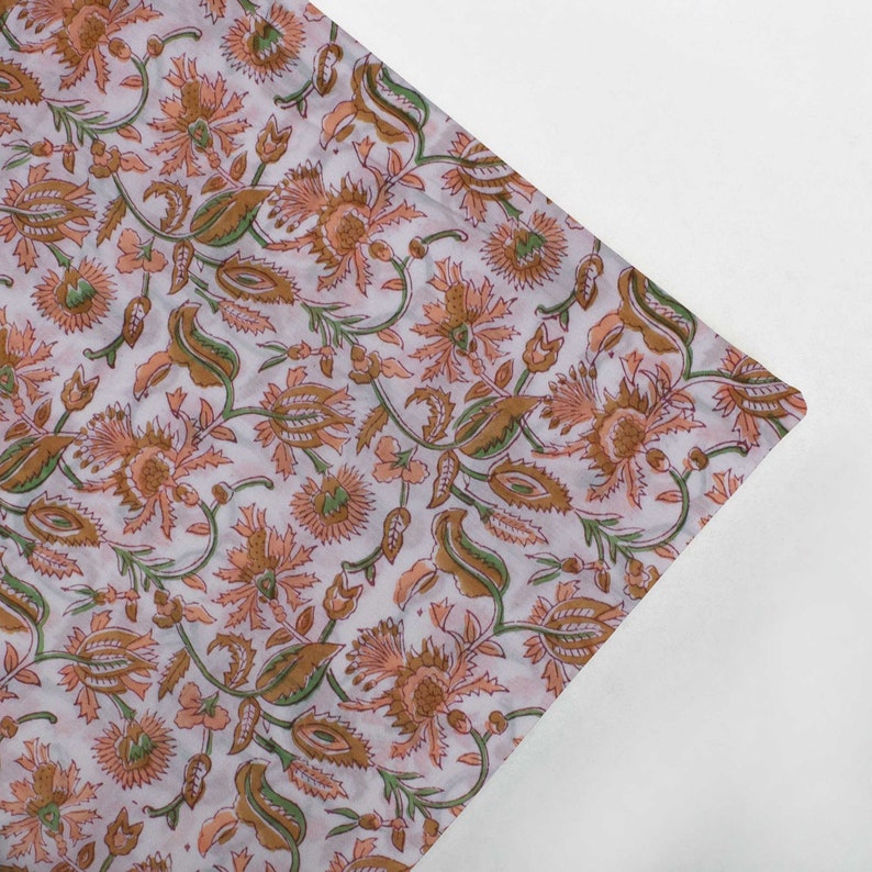 May include: A white fabric with a floral pattern in shades of peach and green. The fabric has a delicate, hand-printed look.
