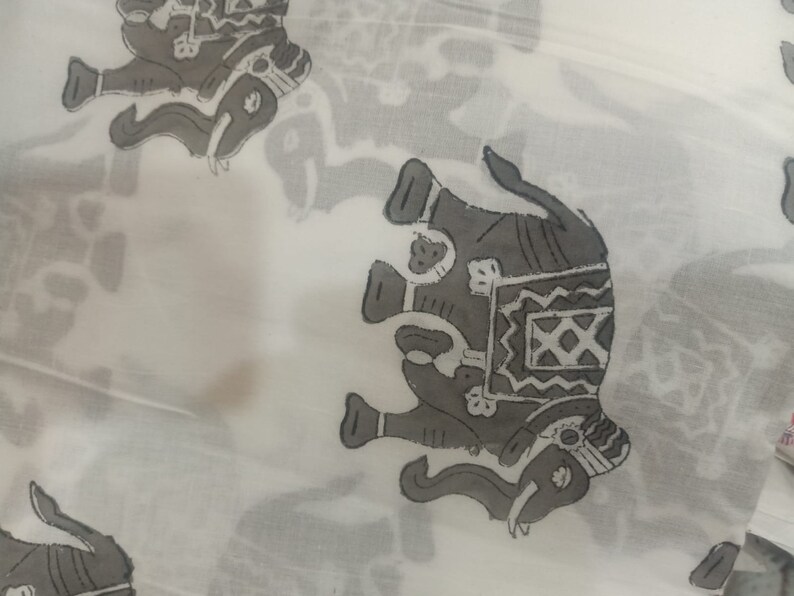 May include: White fabric with a repeating pattern of gray elephants. The elephants are stylized and have intricate designs on their backs.