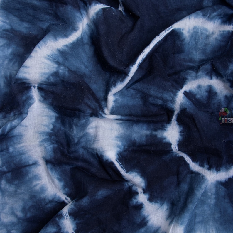 May include: A close-up of a blue and white tie-dye fabric. The fabric is wrinkled and has a soft, textured feel.
