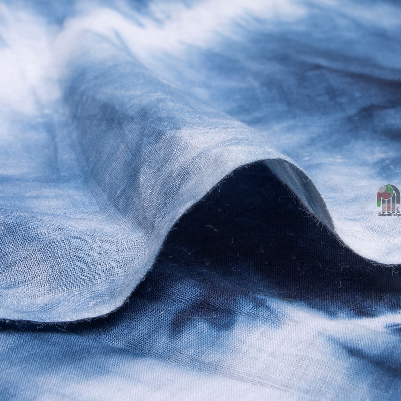 May include: Close-up of a blue and white tie-dye fabric. The fabric is soft and textured, with a subtle sheen.