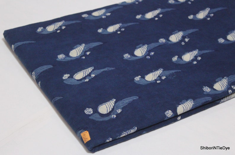 K&ouml;nnte beinhalten: Indigo blauer Baumwollstoff mit einem wei&szlig;en Blumenmuster. Der Stoff ist in der H&auml;lfte gefaltet und hat ein kleines Etikett mit dem Text "ShiboriNTieDye".