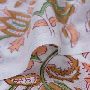 May include: White fabric with a floral print in shades of peach, brown, and green. The fabric is folded over, showing the pattern on both sides.