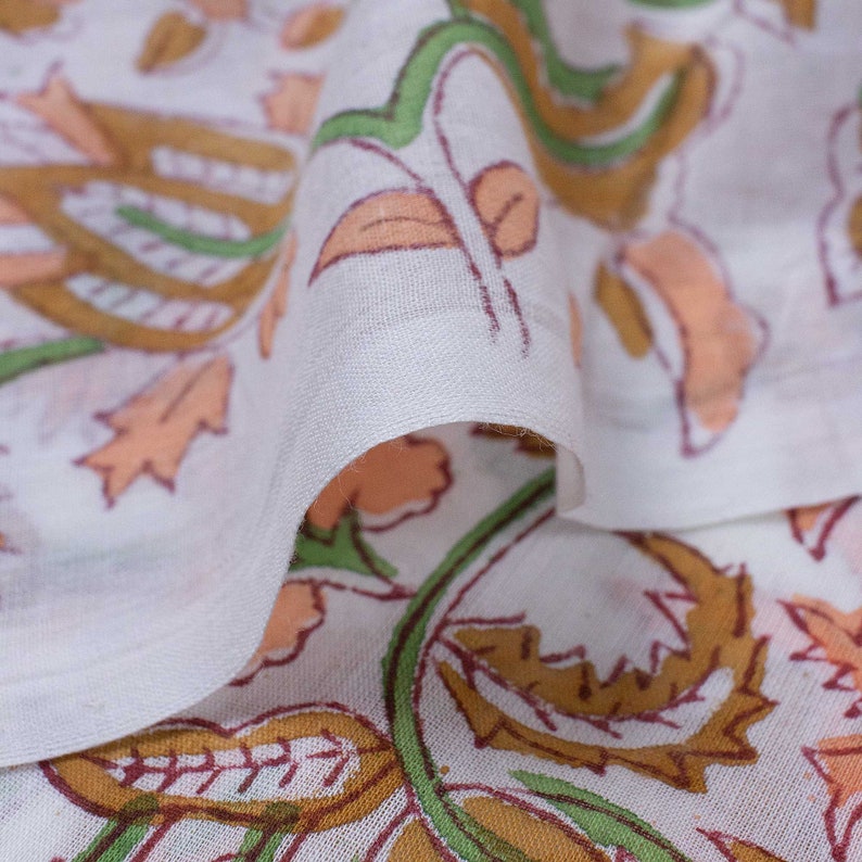 May include: White fabric with a floral print in shades of peach, brown, and green. The fabric is folded over, showing the pattern on both sides.