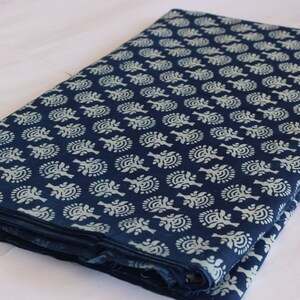 May include: A folded piece of indigo blue cotton fabric with a white floral pattern. The fabric is folded in thirds and has a white tag with the text "ShiboriNTieDye" on the bottom right corner.