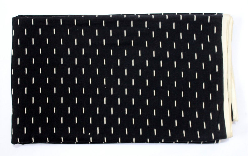 May include: Black fabric with a white ikat pattern. The fabric has a white border.