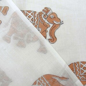 May include: White cotton fabric with a brown elephant print. The elephant has a patterned design on its body and a crown on its head.