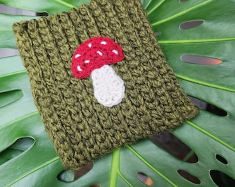 May include: A green crocheted pouch with a white and red mushroom design. The pouch is made of yarn and has a textured surface.