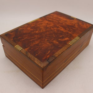 May include: A wooden box with a burl wood top and brass accents. The box has a rich brown color and a smooth finish.