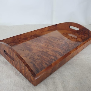 Peut inclure: Un plateau de service rectangulaire en bois avec une finition brillante. Le plateau est de couleur marron chaud avec un motif de grain de bois unique. Il comporte des côtés incurvés avec des poignées découpées. Un objet décoratif pour servir.