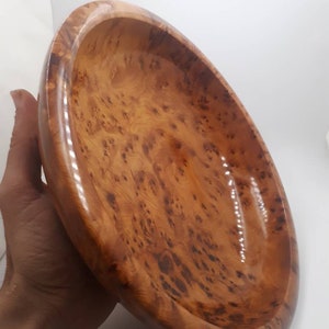 May include: An oval wooden bowl with a polished finish. The bowl is made of light brown wood with dark brown knots and swirls. The interior is smooth and glossy. The bowl is held in a hand.